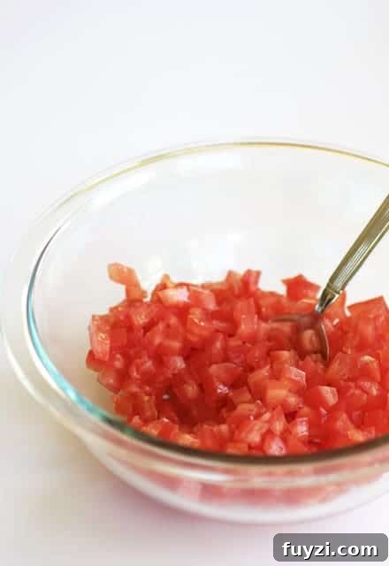 Photo of diced tomatoes in glass mixing bowl being stirred with spoon.