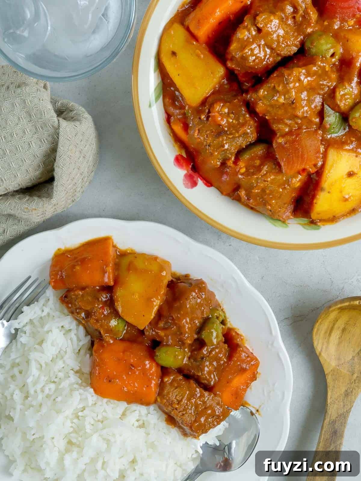 Beef Caldereta with white rice on a white plate with spoon and fork