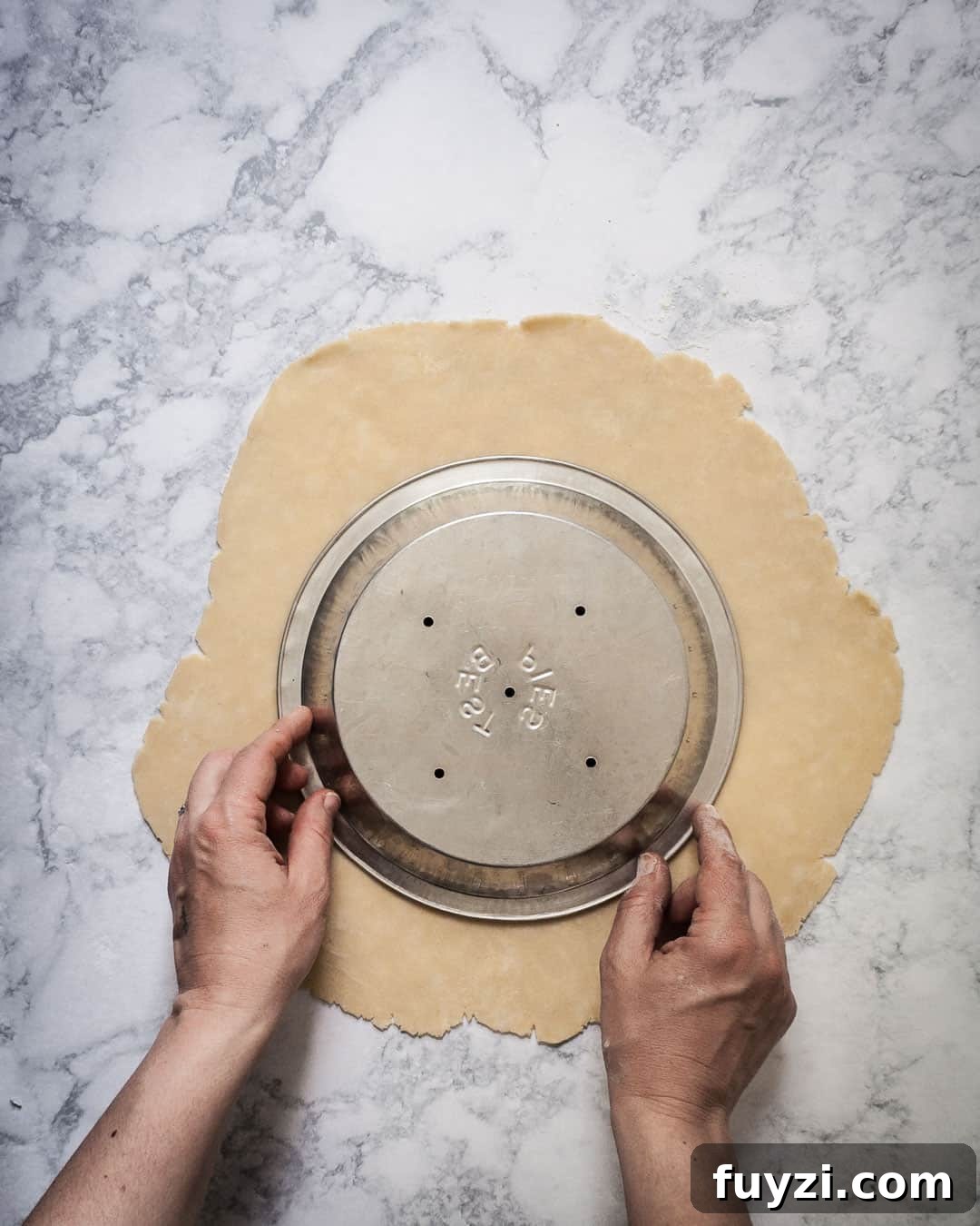Pie crust with two hands placing a pie tin over the top to check the size of the crust.