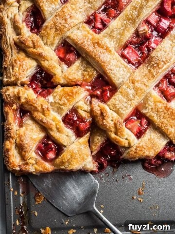 A slice of strawberry rhubarb slab pie being cut out on a baking sheet.