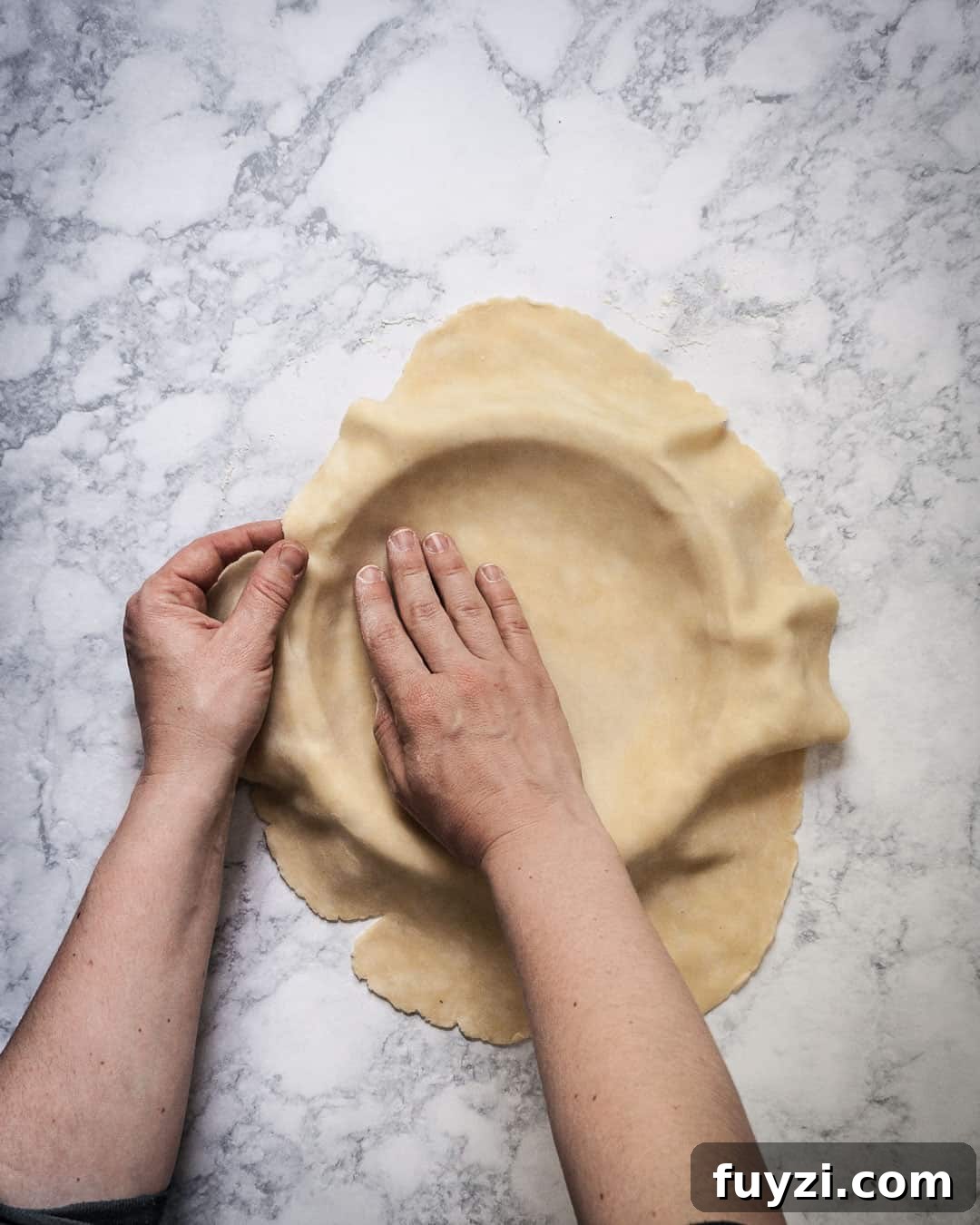 Hands pressing pie dough into a pan.