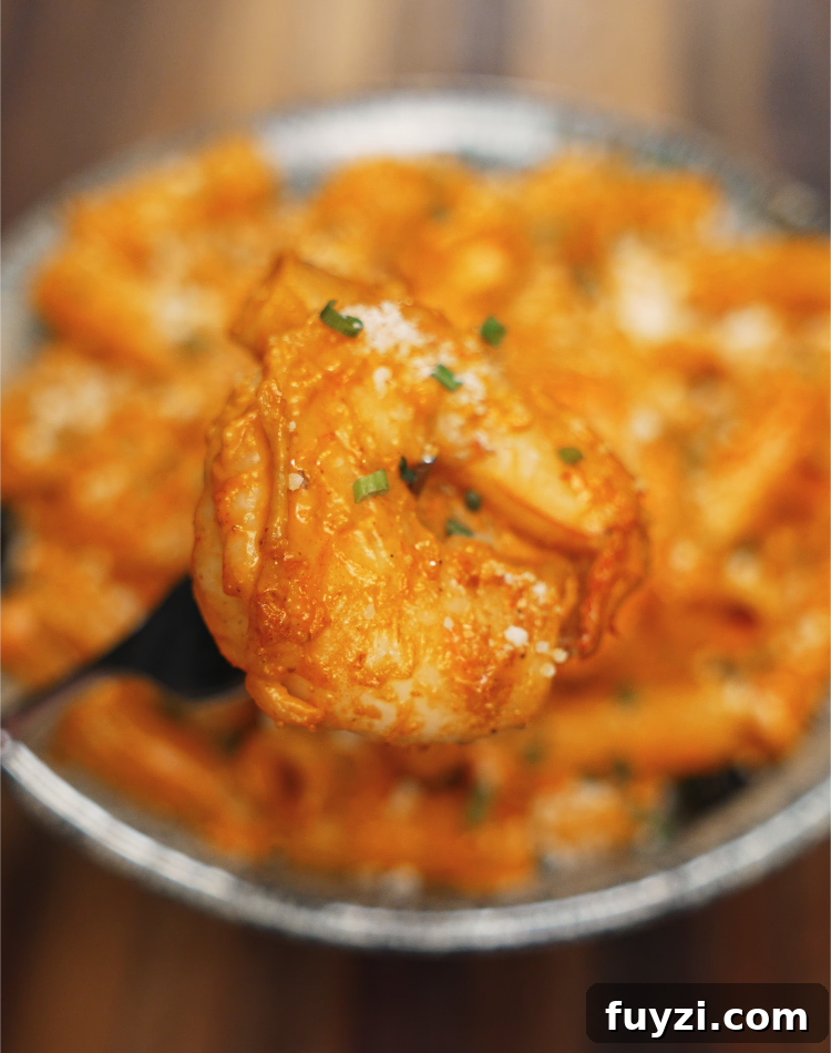 Creamy Spicy Shrimp Pasta Recipe with Garlic Butter 3 A plump shrimp coated in creamy, spicy sauce is held by a fork above a bowl of rigatoni. The shrimp is tender, golden, and dusted with parmesan and herbs for a flavorful finish.