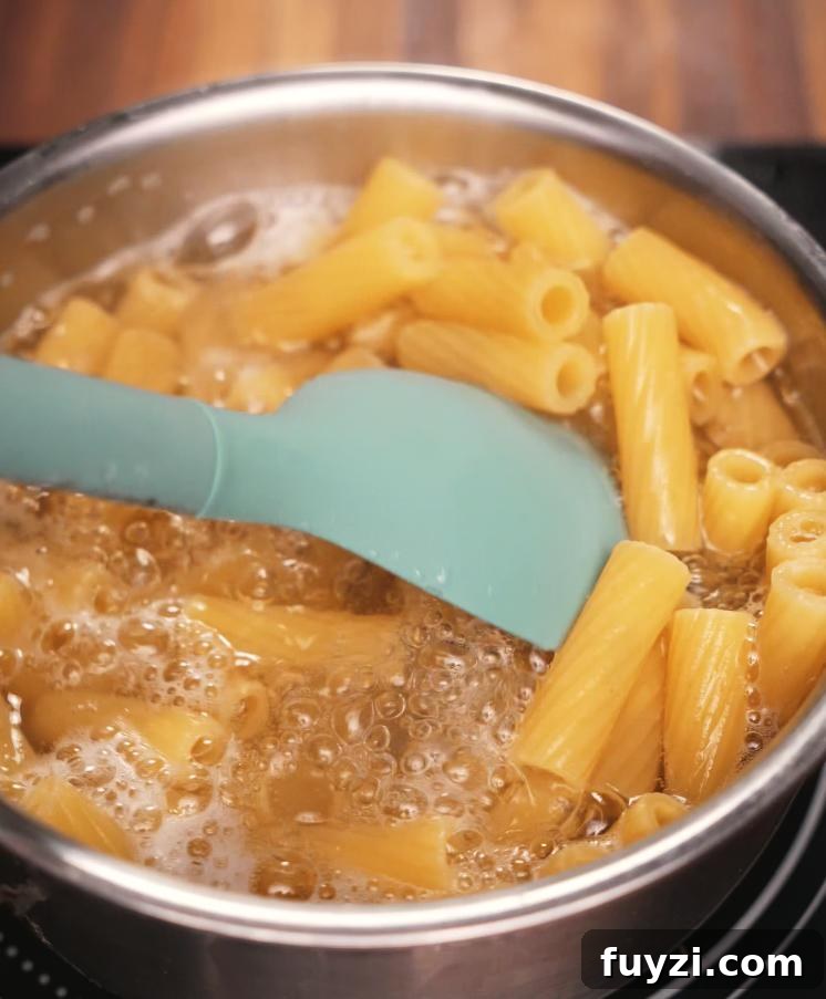 Creamy Spicy Shrimp Pasta Recipe with Garlic Butter 4 Rigatoni pasta boiling in a pot of salted water, stirred with a spatula to prevent sticking, capturing the essential step of cooking pasta for the dish.