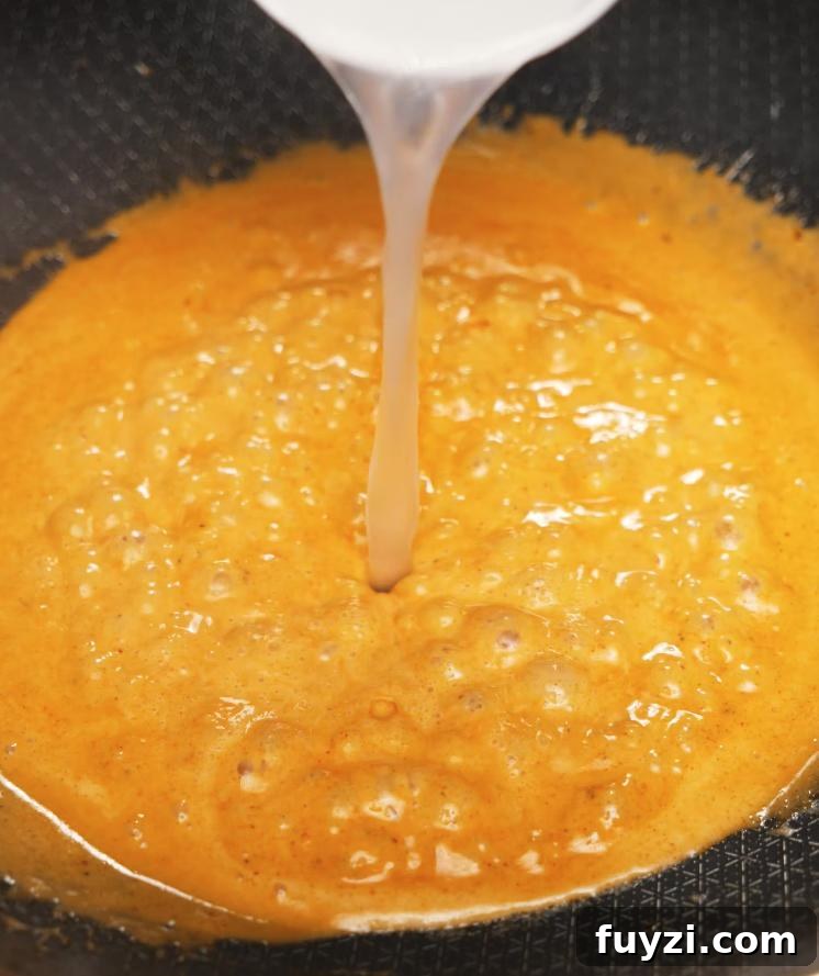 Creamy Spicy Shrimp Pasta Recipe with Garlic Butter 5 Pasta water being poured into a bubbling, spicy butter sauce in a pan, creating the creamy base for the spicy shrimp pasta sauce.