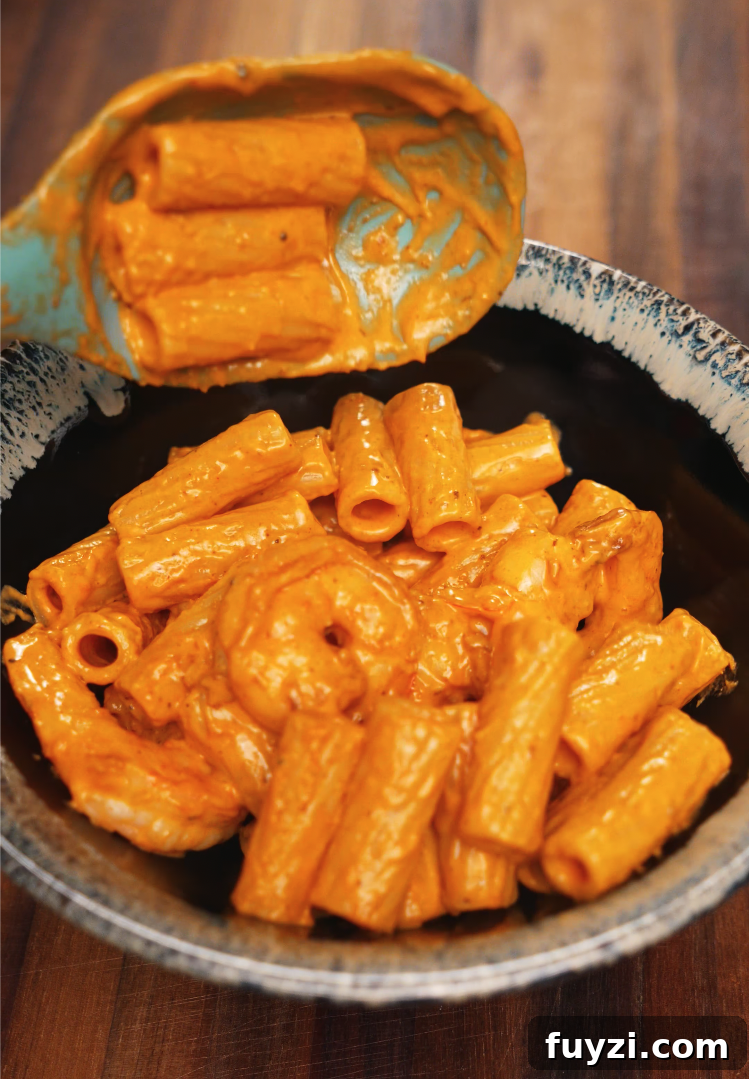 Creamy Spicy Shrimp Pasta Recipe with Garlic Butter 6 A spoonful of creamy rigatoni and shrimp is lifted over a bowl, coated in a rich, spicy orange sauce made with chili flakes, garlic, and cream. The glossy finish on the pasta highlights its velvety texture and bold flavor.
