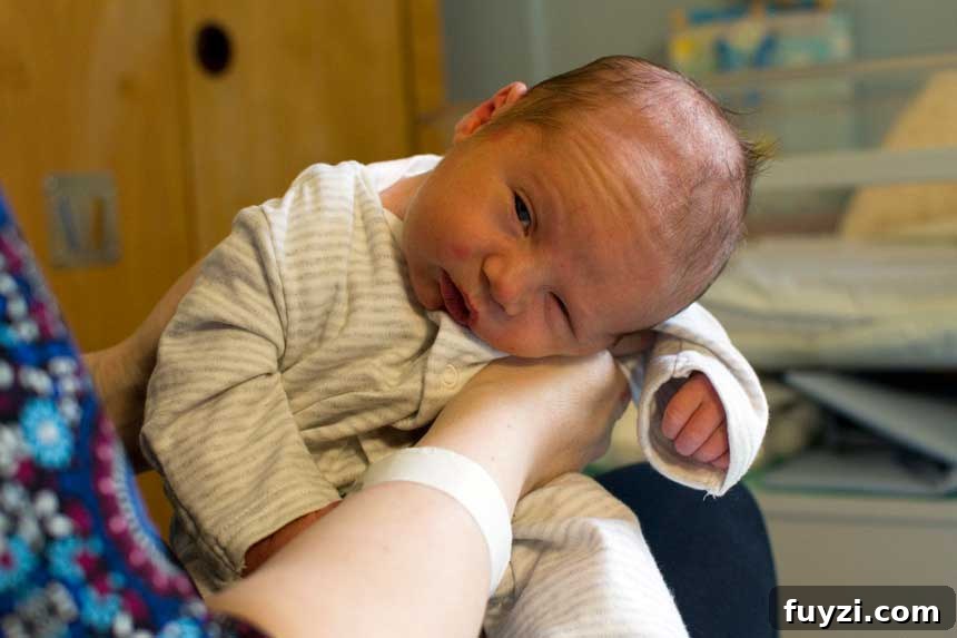 A sleepy newborn baby being held up by mum.