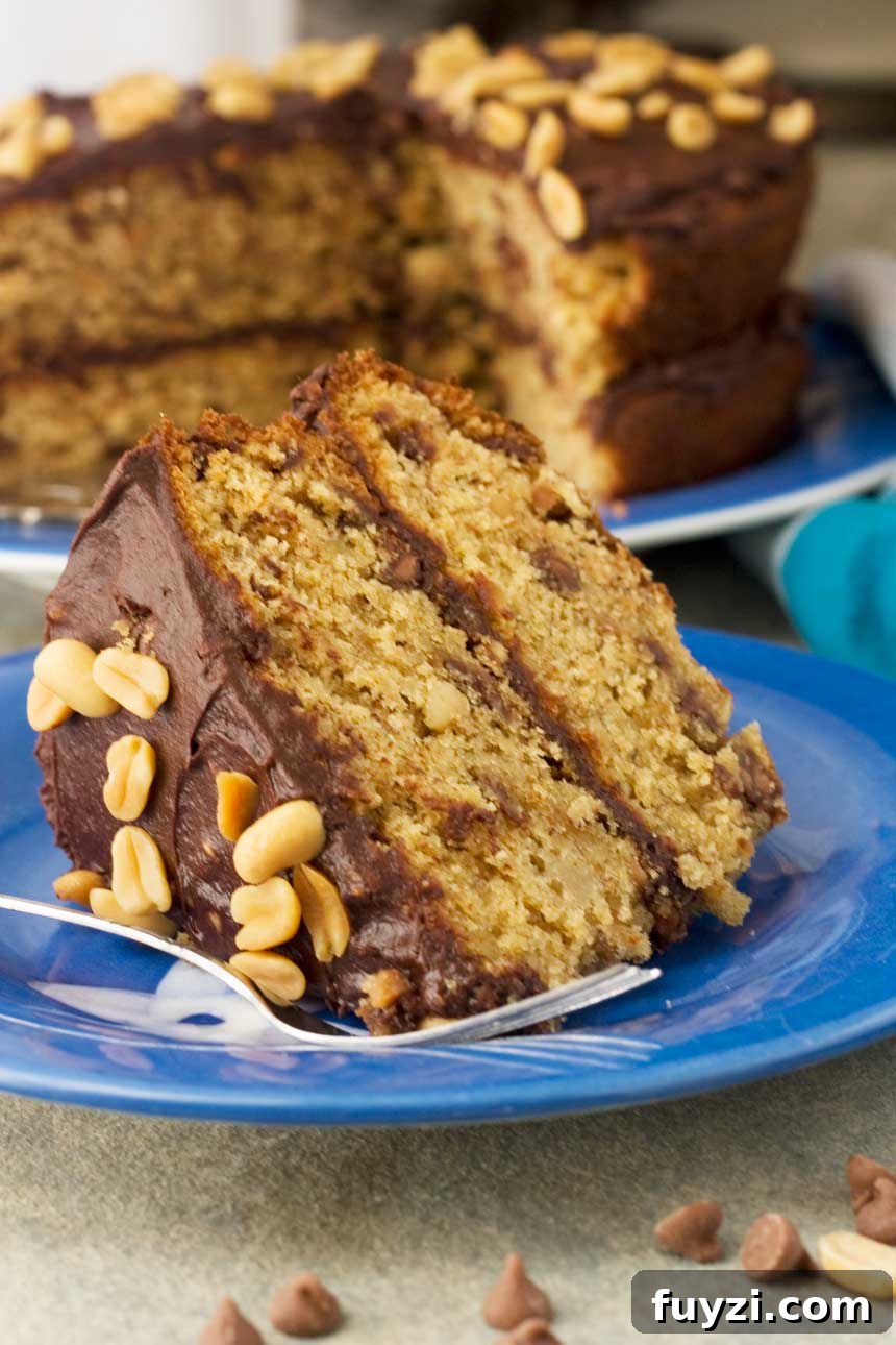 A big slice of peanut butter, banana and chocolate chip cake on a blue plate with a fork with the whole cake in the background.