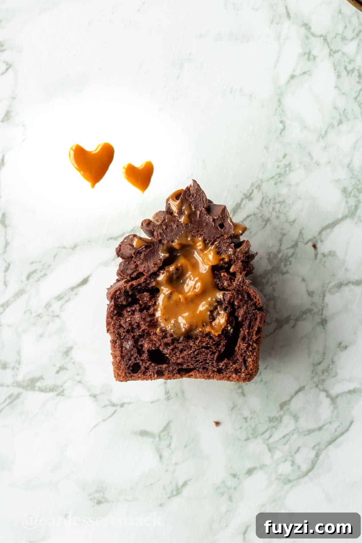 Gooey Chocolate Caramel-Filled Cupcakes Recipe 10 Half section of a chocolate dulce de leche cupcake with 2 caramel hearts on marble countertop.