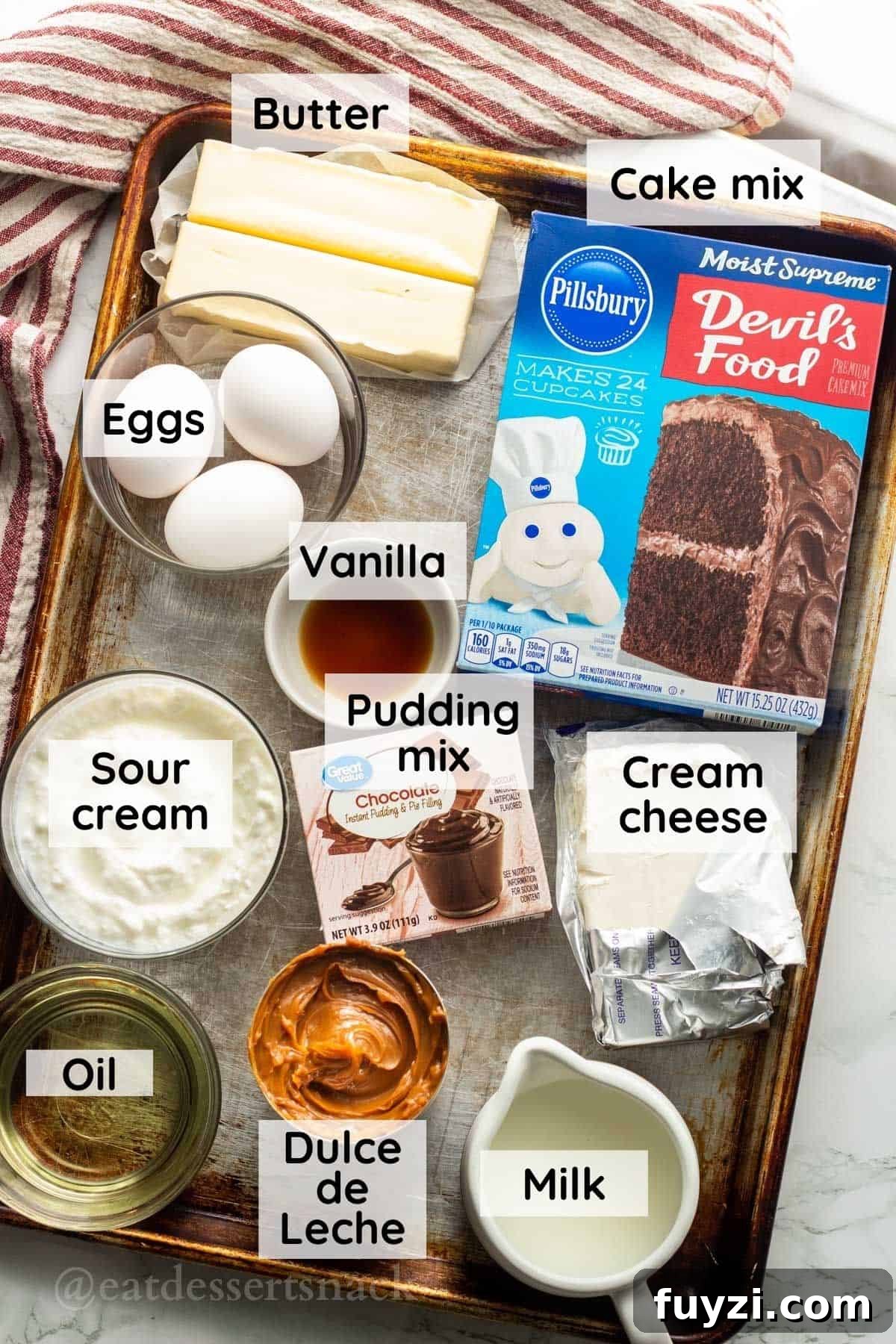 Gooey Chocolate Caramel-Filled Cupcakes Recipe 3 Butter, eggs, vanilla, chocolate pudding, cake mix, cream cheese, milk, oil, and caramel on metal baking sheet.
