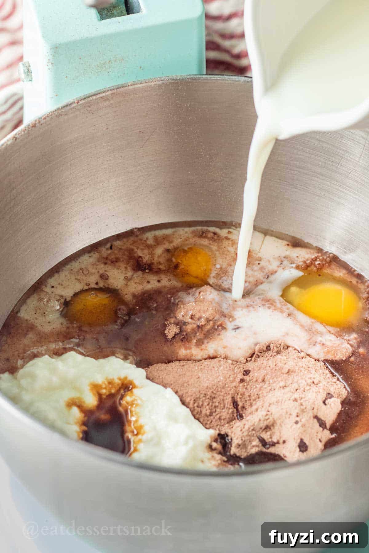 Gooey Chocolate Caramel-Filled Cupcakes Recipe 4 Milk pouring into metal mixing bowl with cake batter, eggs, vanilla, and sour cream.