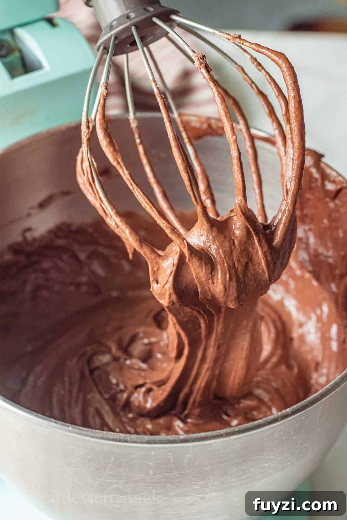 Gooey Chocolate Caramel-Filled Cupcakes Recipe 5 Metal whisk with chocolate cake batter on it above metal mixing bowl.