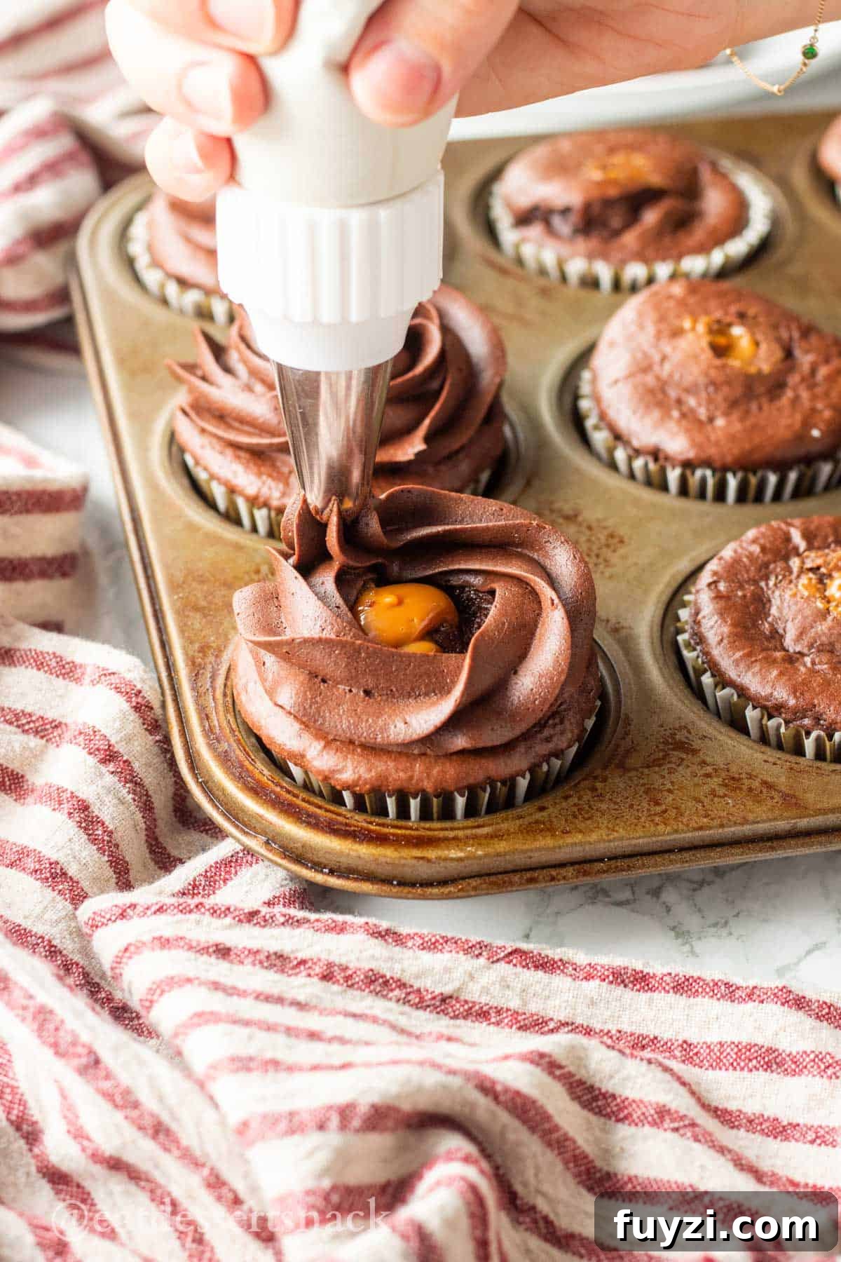 Gooey Chocolate Caramel-Filled Cupcakes Recipe 7 Hand piping chocolate frosting onto caramel filled chocolate cupcakes.