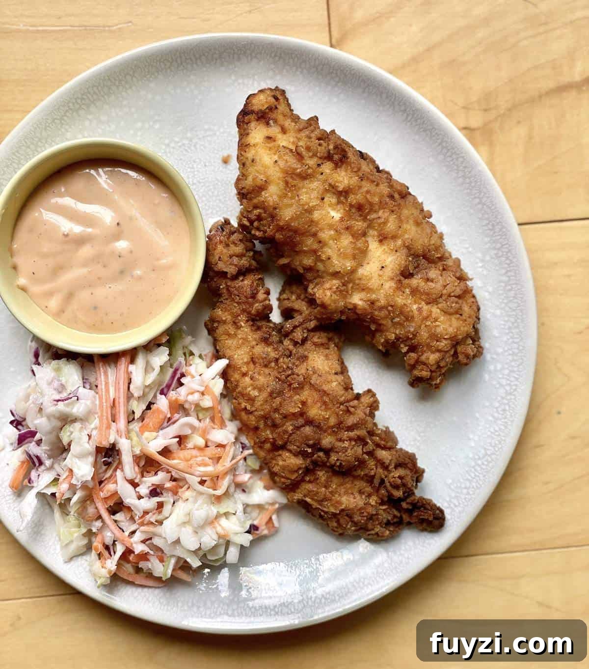 Two homemade raising canes chicken tenders, canes sauce, and canes coleslaw on a white plate.