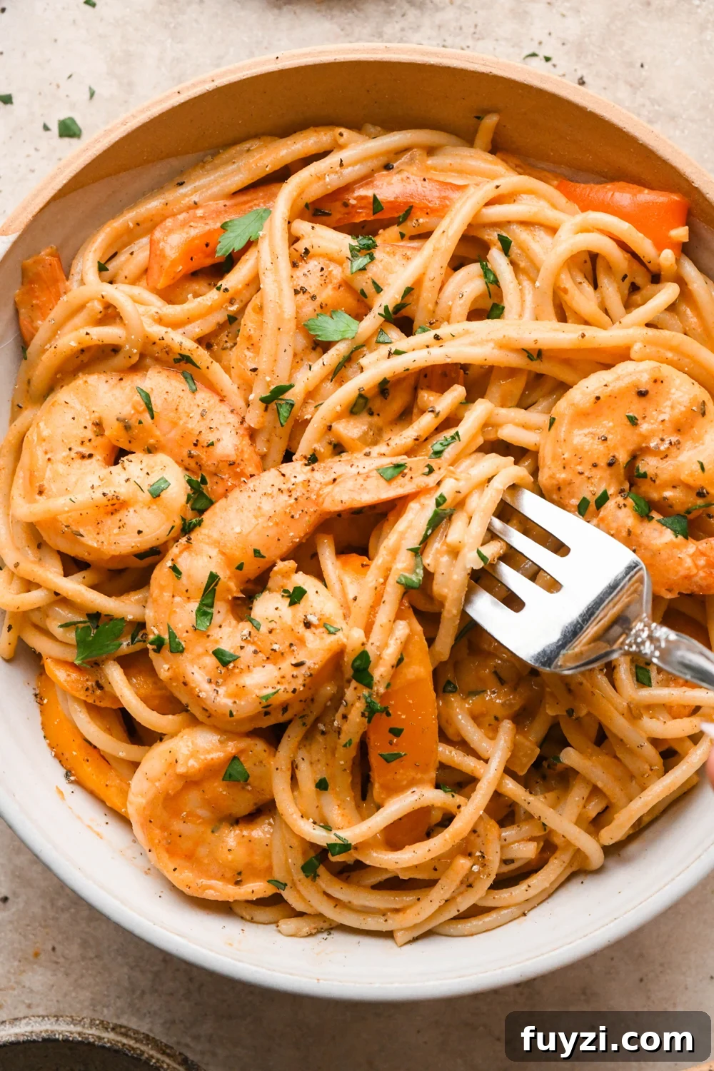 A ceramic bowl of dairy free cajun shrimp pasta, garnished with fresh parsley and black pepper. A fork is digging into the bowl, twirling a bite of pasta and lifting it up to show the creamy texture of the sauce.