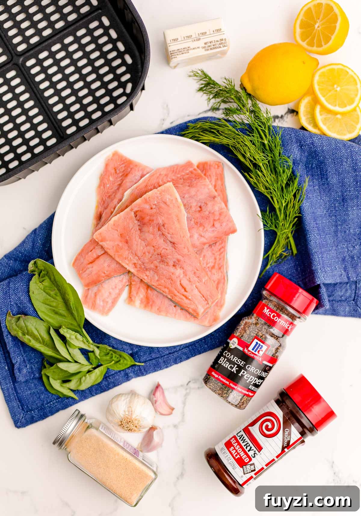Ingredients to make salmon in the air fryer on a marble surface with a blue napkin.