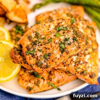 Close up photo of air fryer salmon filets on a white plate with lemon and asparagus in the background.