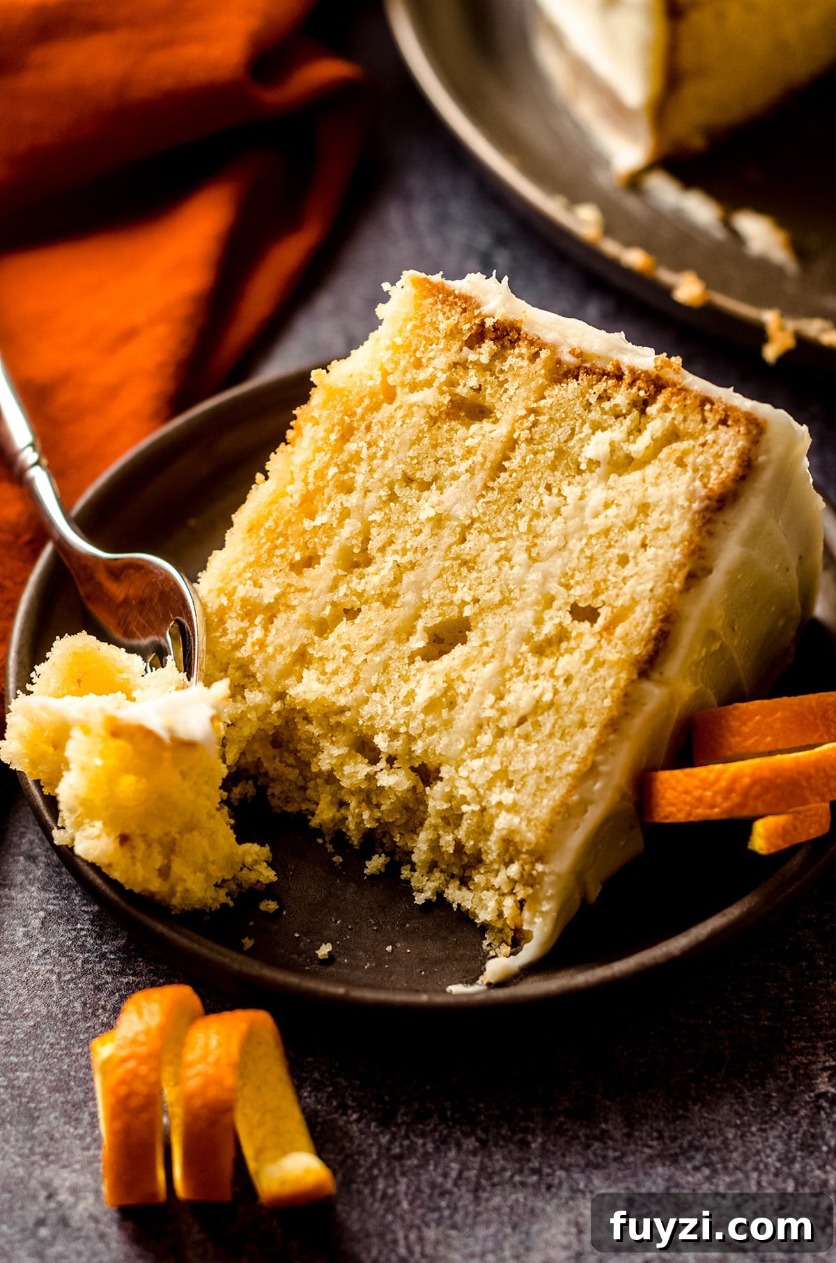 slice of orange creamsicle layer cake on a plate with a fork and a bite taken out of it