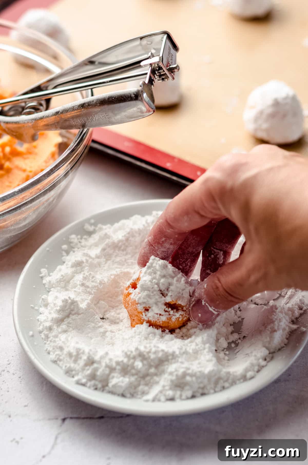 a hand rolling orange creamsicle cookie dough in powdered sugar to make crinkle style cookies