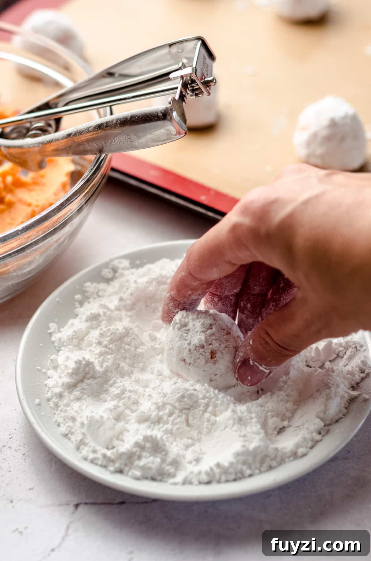 a hand rolling orange creamsicle cookie dough in powdered sugar to make crinkle style cookies