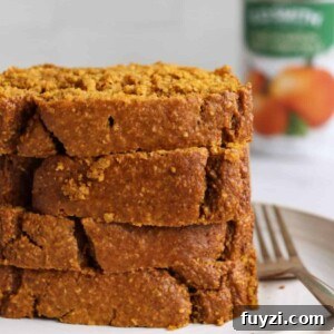 Four slices of gluten free banana bread piled on a white plate with a gold fork.