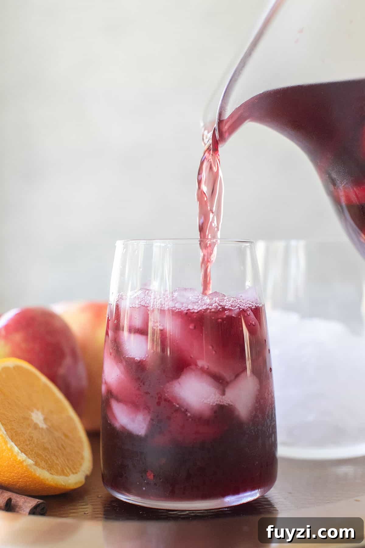 Spiced Autumn Apple and Pear Sangria Recipe 7 Sangria being poured into a wine glass filled with ice.