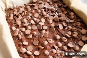 Fudgy Chunky Chocolate Chip Brownies Recipe 9 Chocolate chips sprinkled over the brownie mixture in a baking tray lined with brown parchment paper
