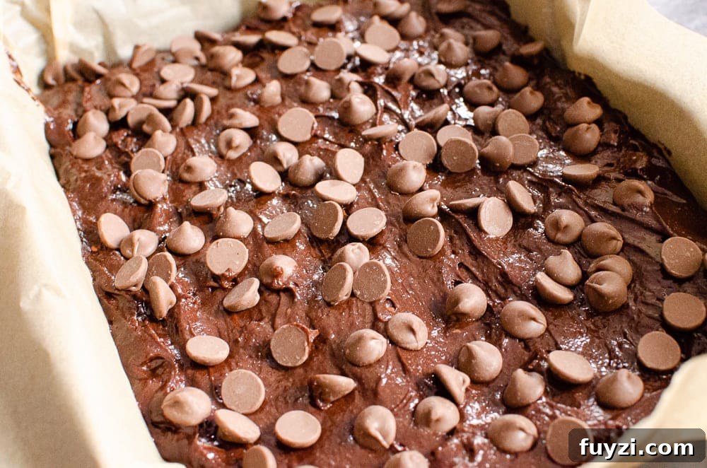 Fudgy Chunky Chocolate Chip Brownies Recipe 18 Chocolate chips sprinkled over the brownie mixture in a baking tray lined with brown parchment paper