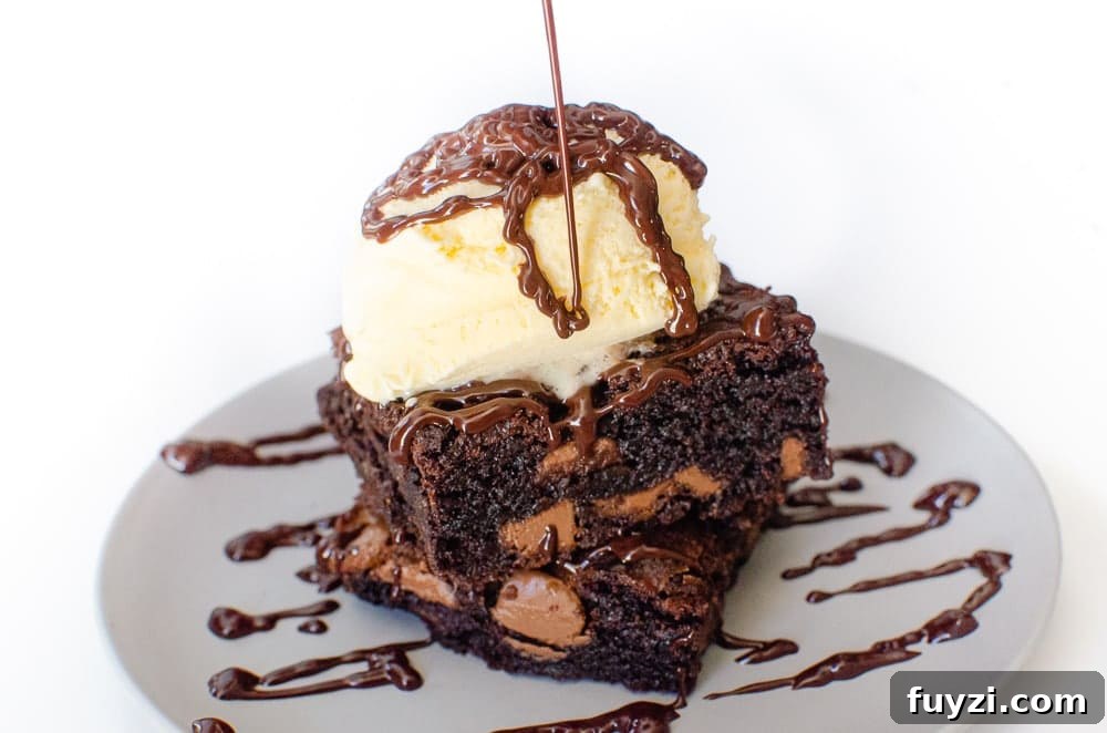 Fudgy Chunky Chocolate Chip Brownies Recipe 22 Chunky Chocolate Chip Brownies on a grey plate drizzled with chocolate sauce and vanilla ice cream on top