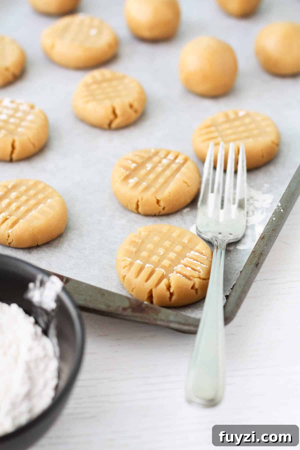 Classic Peanut Butter Cookie Recipe with Natural Peanut Butter 11 Pressing scoops of peanut butter cookie dough with a fork before baking.