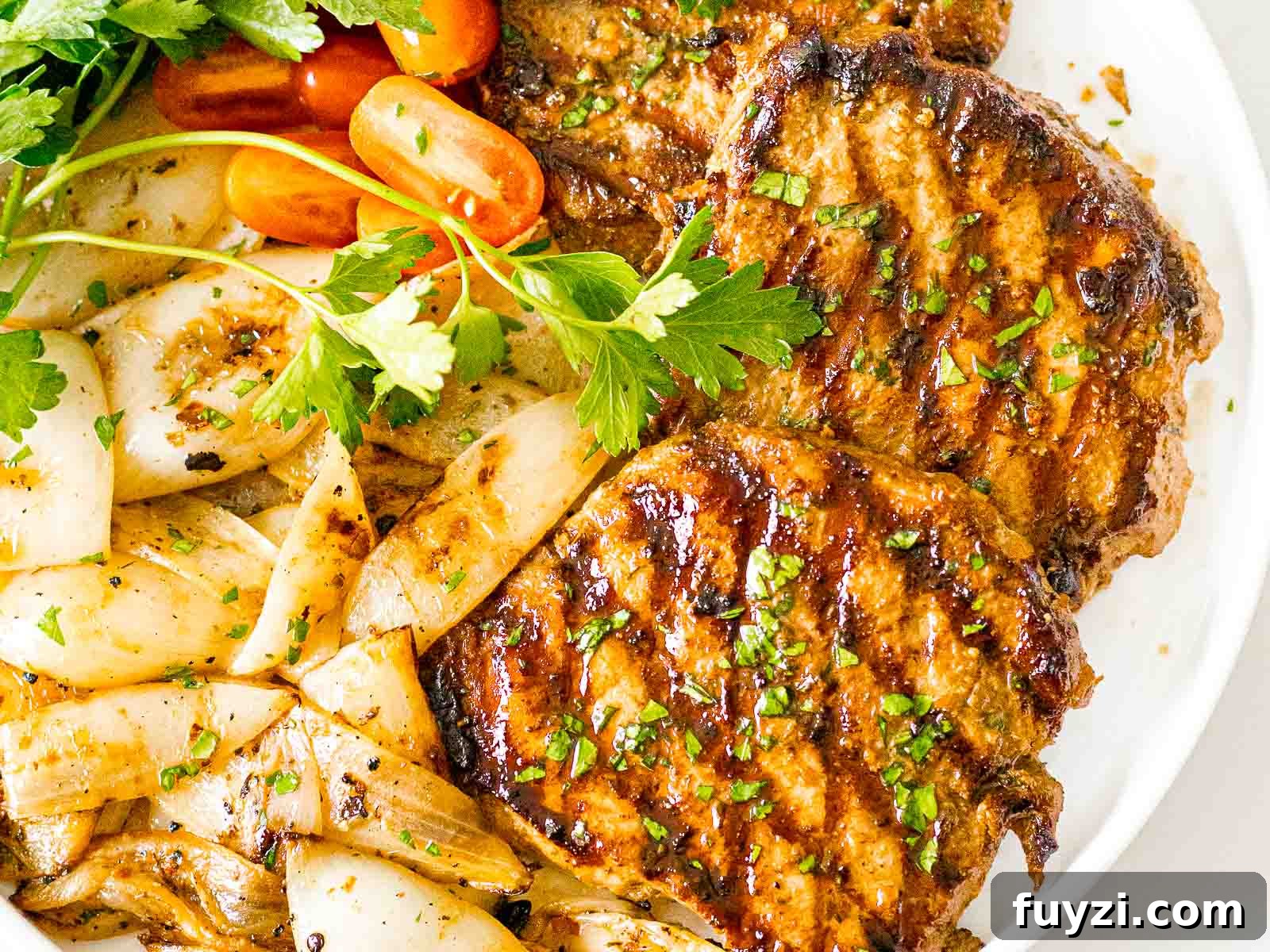 savory grilled pork chops on a white plate next to grilled onions and tomatoes