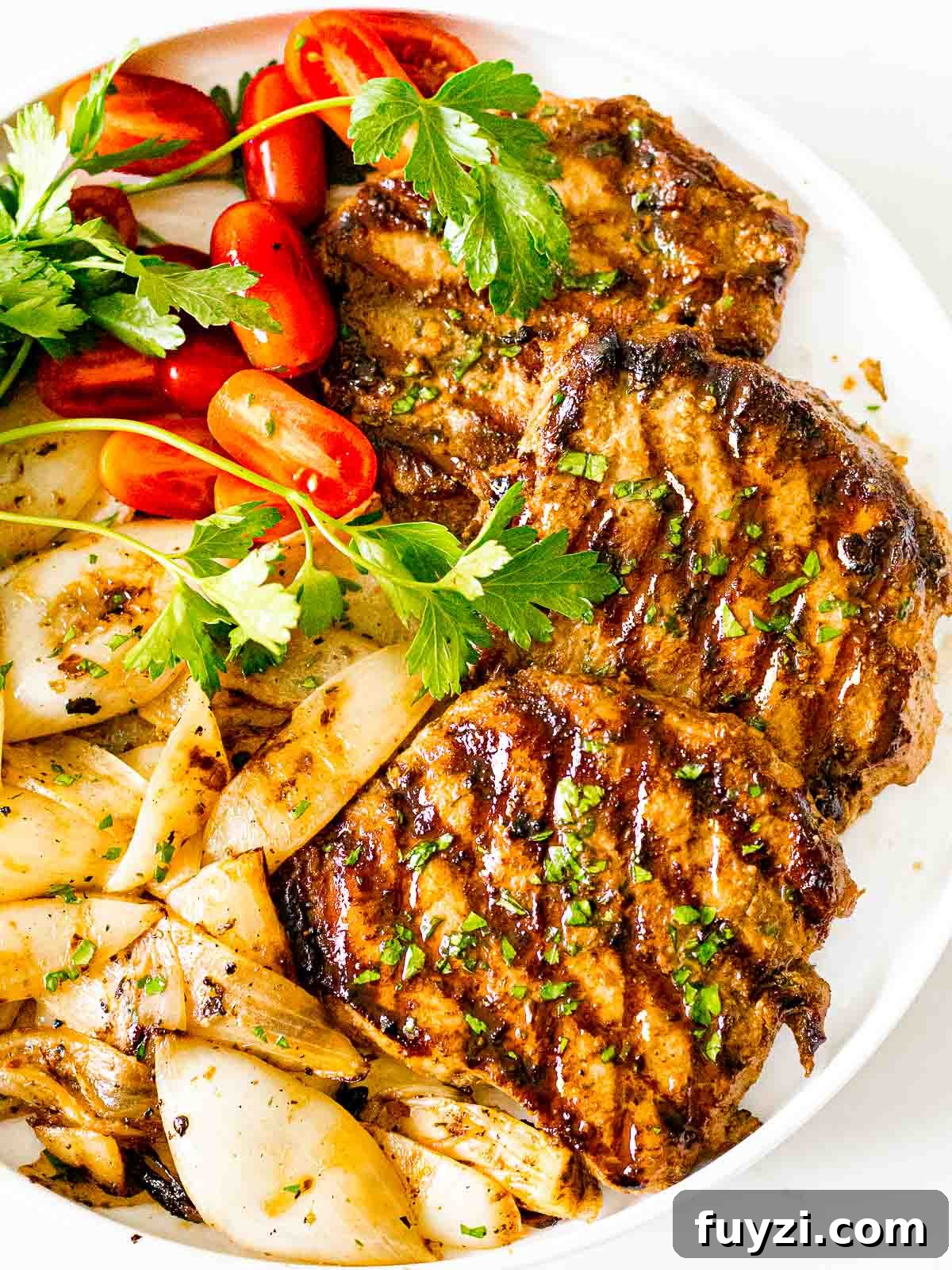 juicy grilled pork chops with grill marks on a white plate next to grilled onions and tomatoes