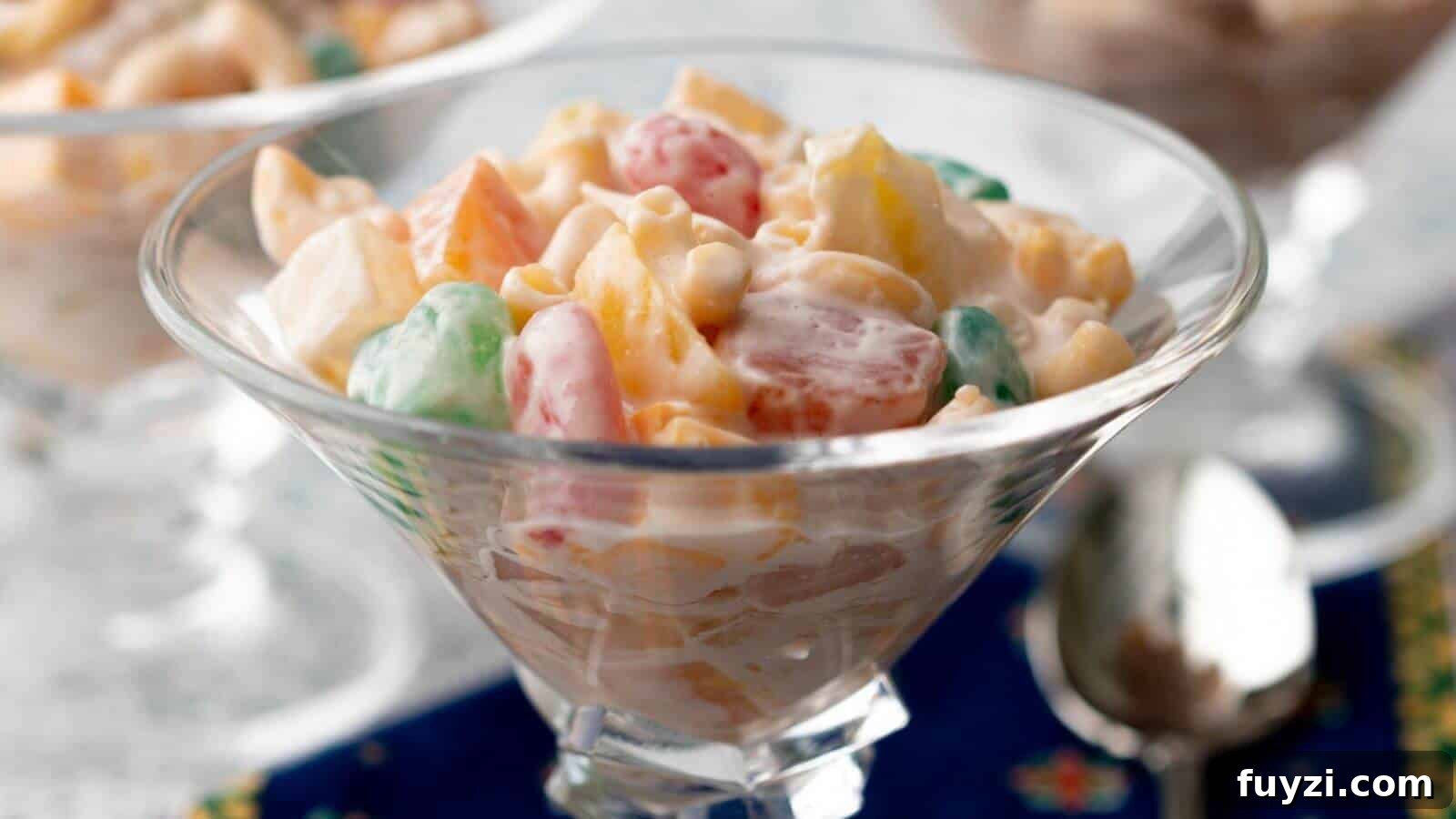 27 Crowd-Pleasing Outdoor Potluck Recipes for Late Summer 12 A glass bowl filled with a creamy fruit salad, featuring colorful fruits and marshmallows, placed on a blue cloth.