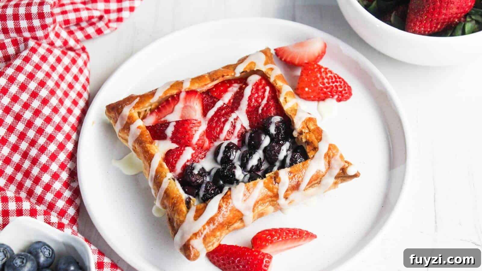 27 Crowd-Pleasing Outdoor Potluck Recipes for Late Summer 13 A pastry with berry filling and white drizzle on a white plate is accompanied by strawberry slices. A red and white checkered cloth, blueberries, and a bowl of strawberries are nearby.