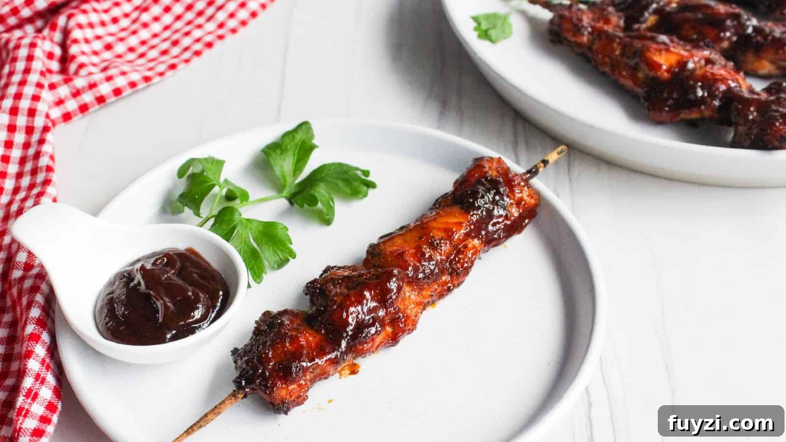 27 Crowd-Pleasing Outdoor Potluck Recipes for Late Summer 16 A single barbecued chicken skewer on a white plate, with a small bowl of barbecue sauce and a parsley garnish, next to a plate of additional chicken skewers.