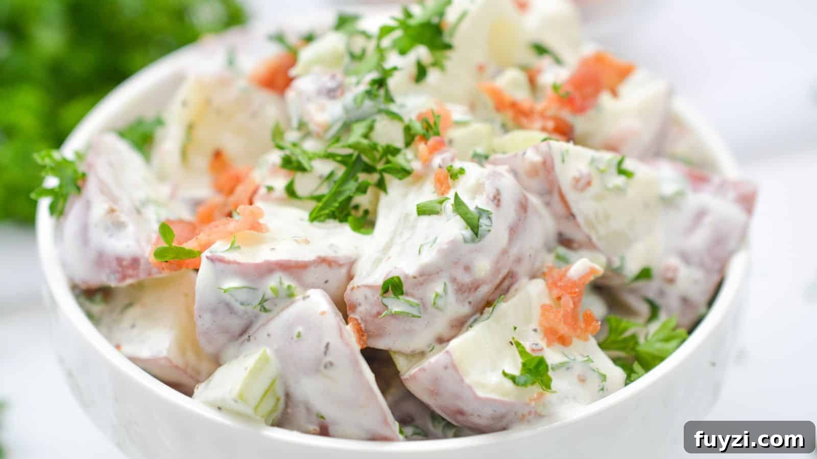 27 Crowd-Pleasing Outdoor Potluck Recipes for Late Summer 24 Bowl of potato salad garnished with fresh herbs and bacon on a white background.