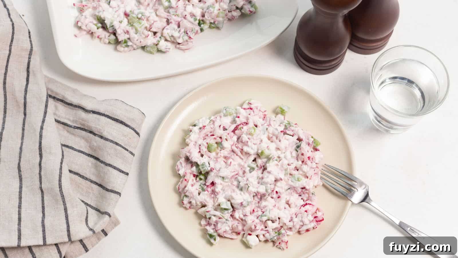 27 Crowd-Pleasing Outdoor Potluck Recipes for Late Summer 25 A plate of radish salad with diced celery and a creamy dressing, accompanied by a glass of water and salt and pepper shakers.