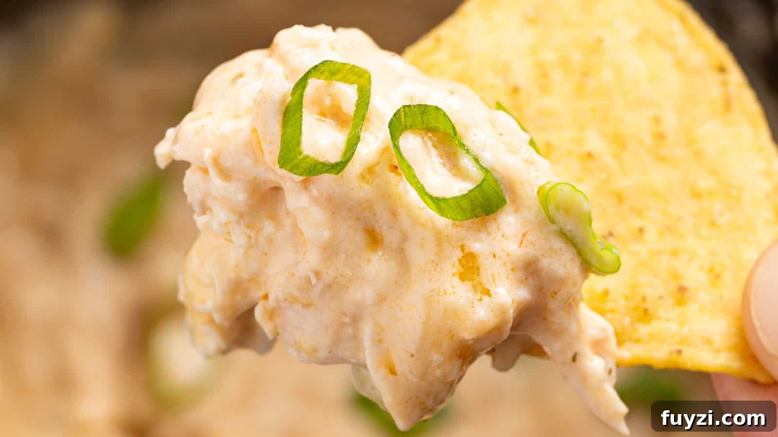 27 Crowd-Pleasing Outdoor Potluck Recipes for Late Summer 26 A hand holding a tortilla chip dipped in creamy Buffalo chicken dip, garnished with slices of green onion.