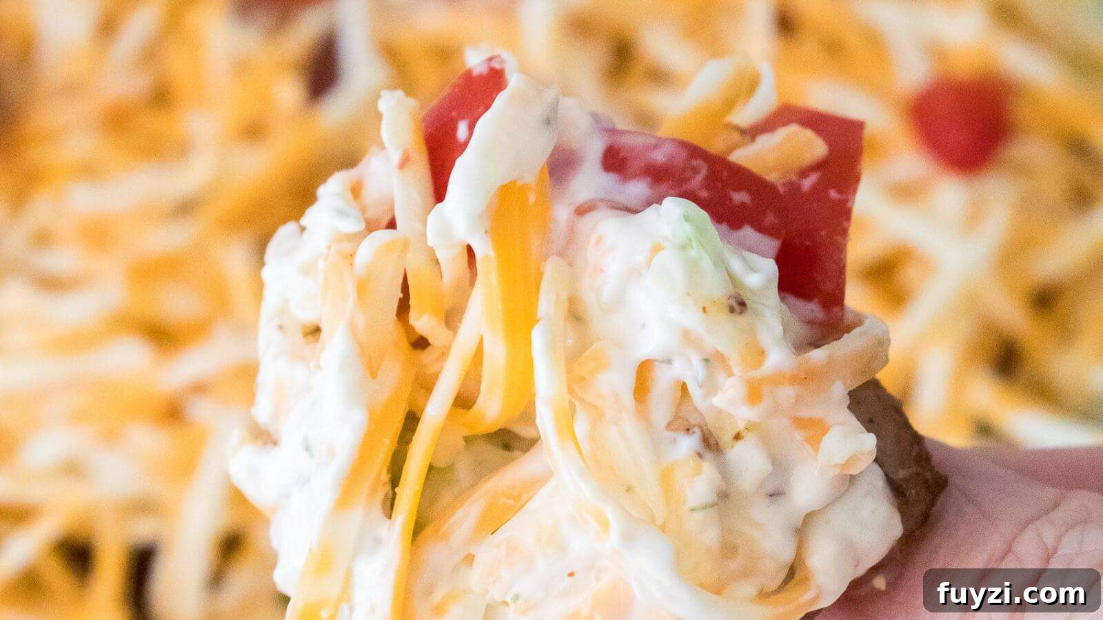27 Crowd-Pleasing Outdoor Potluck Recipes for Late Summer 4 A hand holding a loaded potato skin topped with shredded cheese, sour cream, and a slice of tomato.