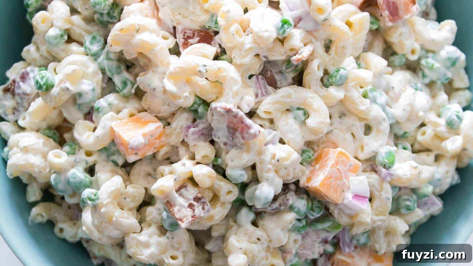 27 Crowd-Pleasing Outdoor Potluck Recipes for Late Summer 5 Close-up of macaroni salad with elbow pasta, peas, cheddar cheese cubes, red onion, and a creamy dressing.