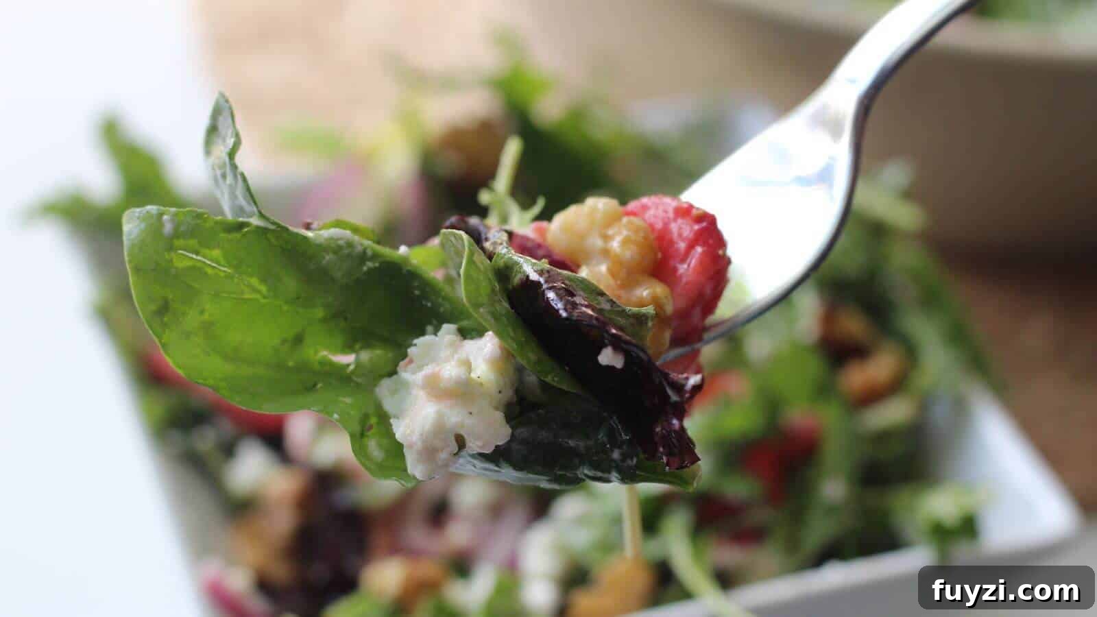 27 Crowd-Pleasing Outdoor Potluck Recipes for Late Summer 9 A fork holds a fresh salad with mixed greens, cherry tomato, walnuts, and crumbled cheese over a bowl of salad in the background.