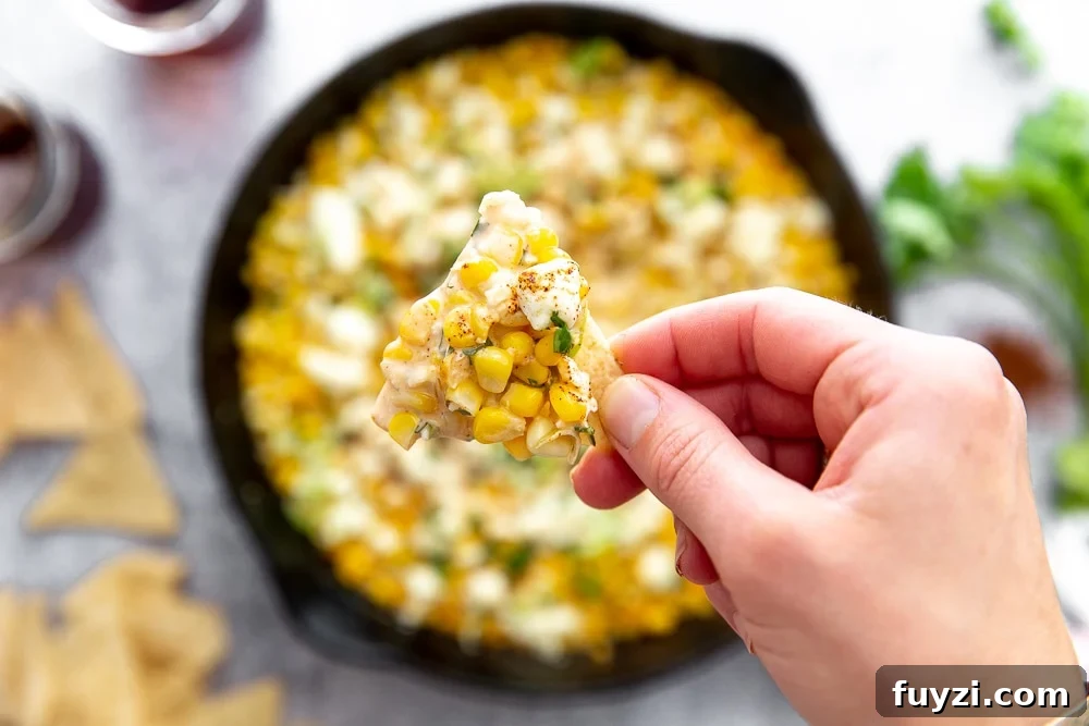 Close up overhead shot of hand holding tortilla chip topped with Mexican street corn dip.