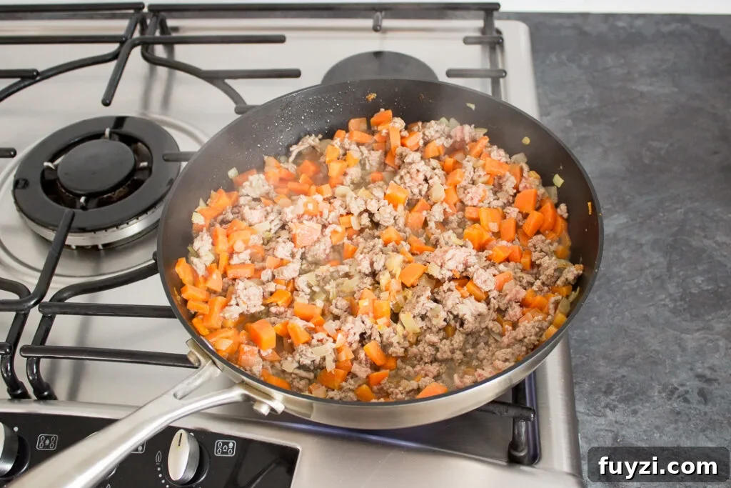Root vegetables and mince cooking in a large frying pan.