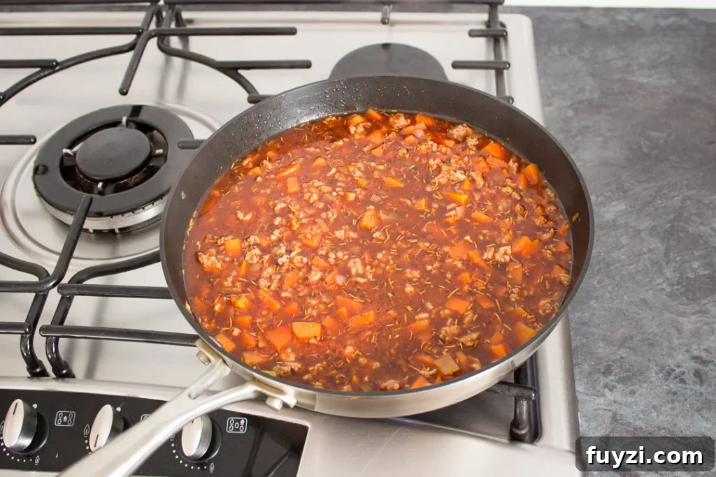 Mince, vegetables, seasonings and beef stock cooking in a large frying pan.