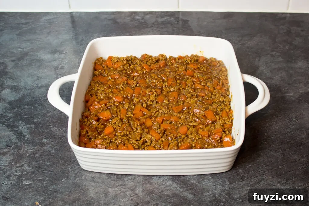 Cooked vegetables and mince in a square white dish.