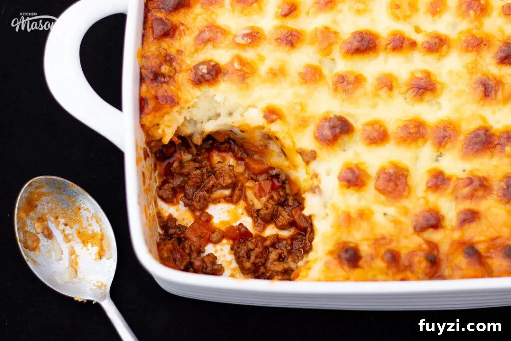 Shepherd's pie in a square white roasting dish with a dirty spoon at the side, and a portion spooned out.