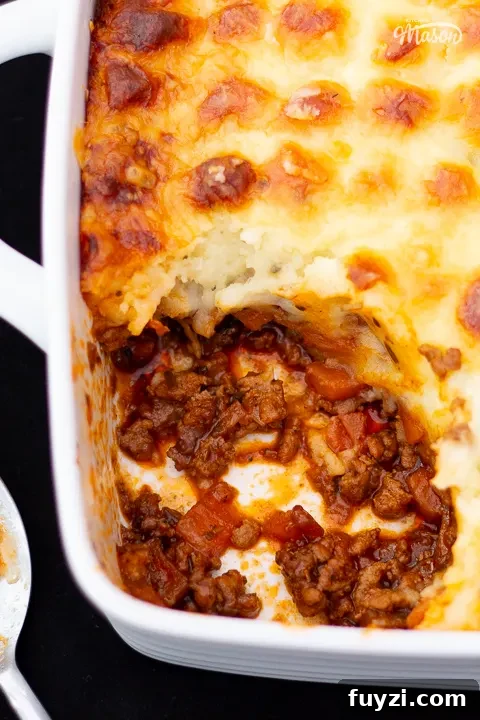 Baked Shepherd's pie in a white dish with a portion spooned out, and a spoon on the side.