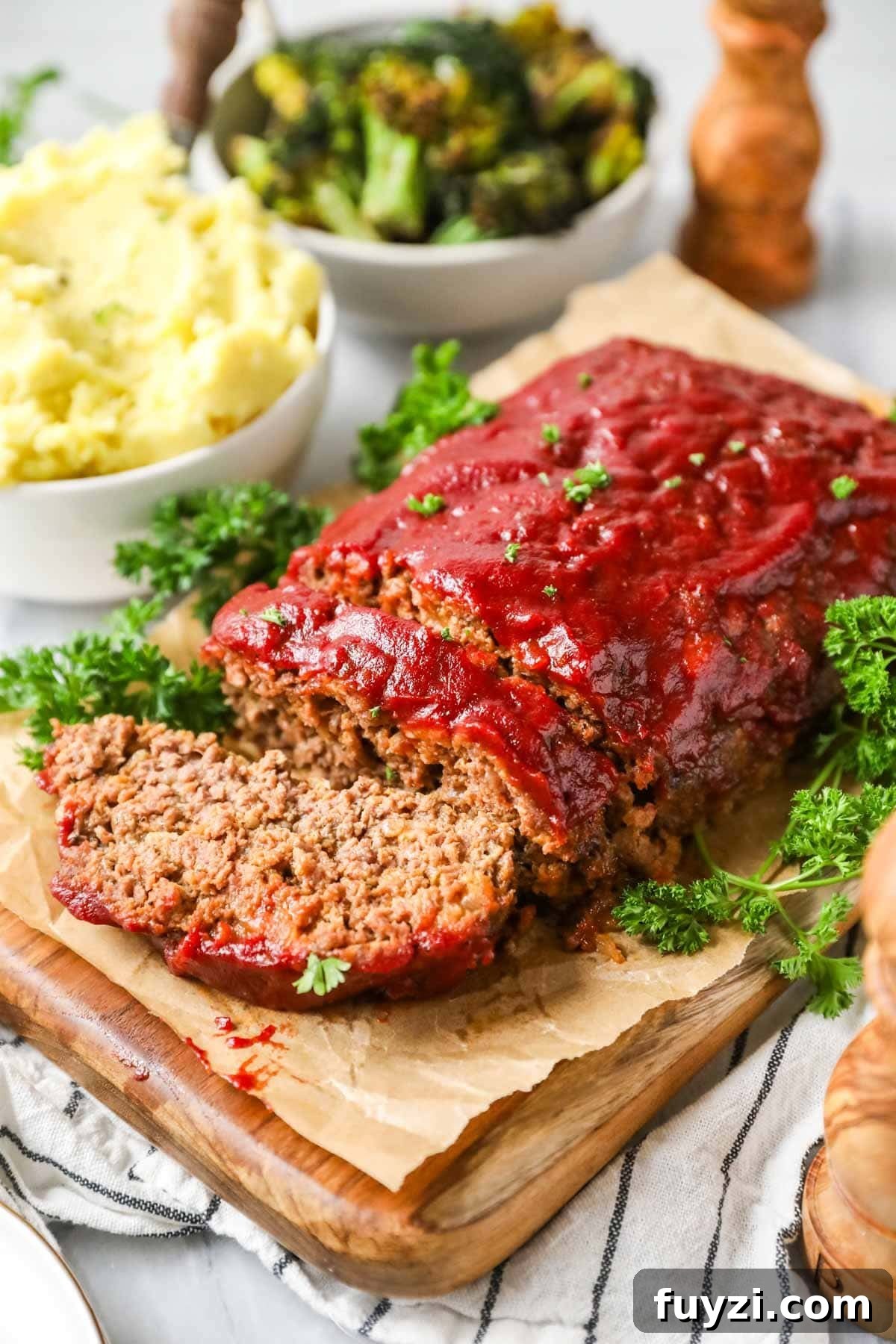 Meatloaf with one slice cut with roasted broccoli and mashed potatoes in the background.