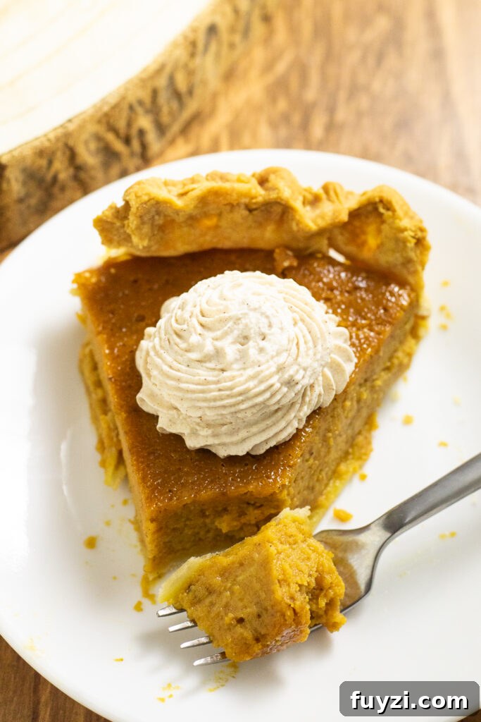 A piece of eggnog pumpkin pie on a small white plate topped with a piped swirl of whipped cream and a fork sitting on the plate with a bite of pie on it.