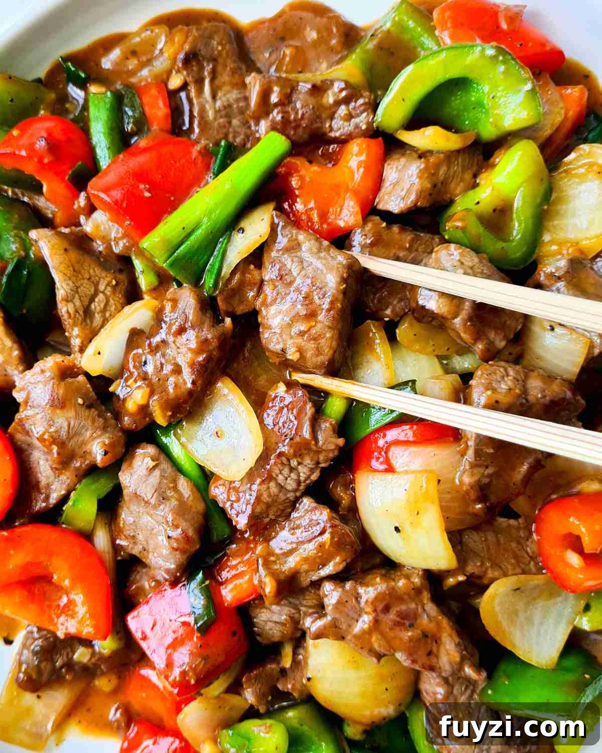 Restaurant-Style Black Pepper Beef Stir-Fry 9 Close up of a piece of beef piece being picked up by a pair of chopsticks