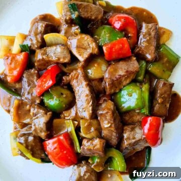Glossy beef and vegetables covered in sauce on a white plate